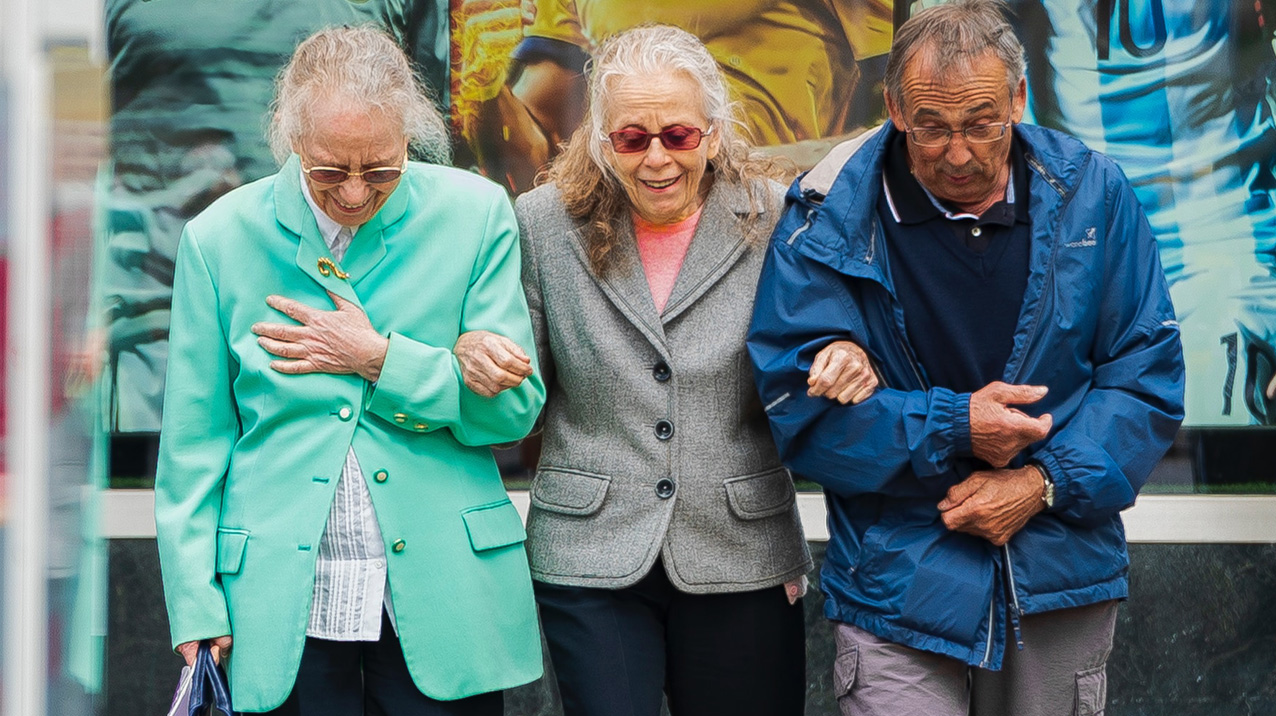 Drie mensen die arm in arm lopen en de middelste persoon ondersteunen